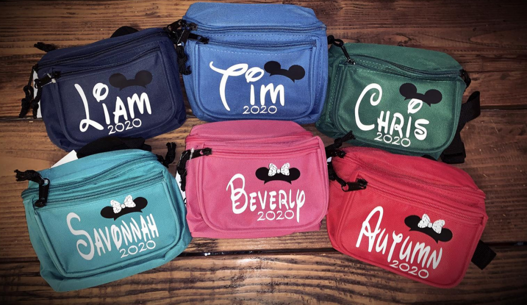 Six different personalized fanny packs, in a variety of colors, with names and year and Mickey ears on them.