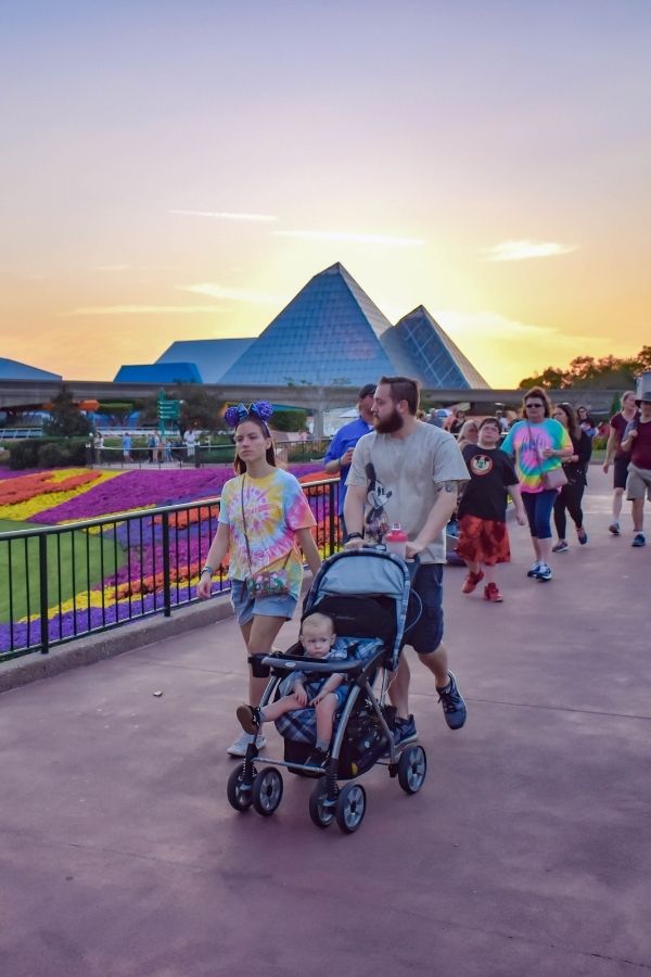 A group of people walking at Epcot in front of the Imagination Pavilion at sunset.