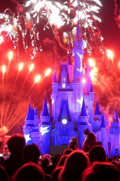Magic Kingdom Cinderella castle at night, lit up with fireworks in the background