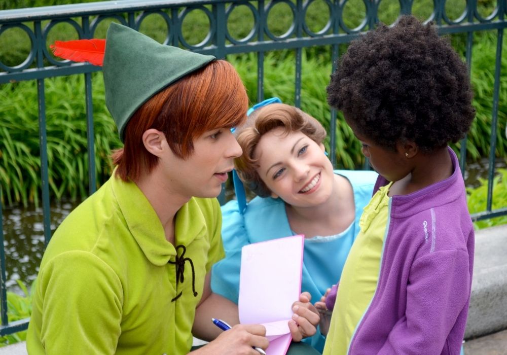 Peter Pan, a male face character at Disney World, greets a young child with Wendy by his side