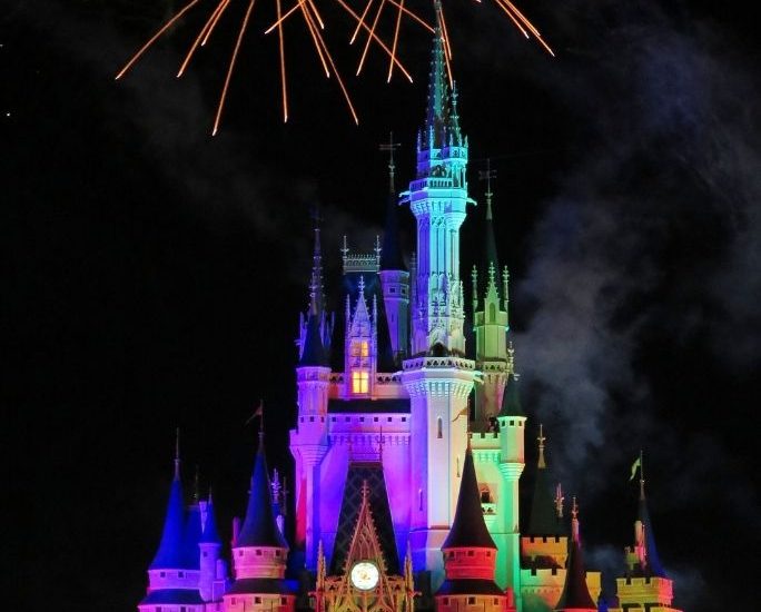 Cinderella's castle in Magic Kingdom at Disney World is lit up with multiple colors as fireworks explode overhead