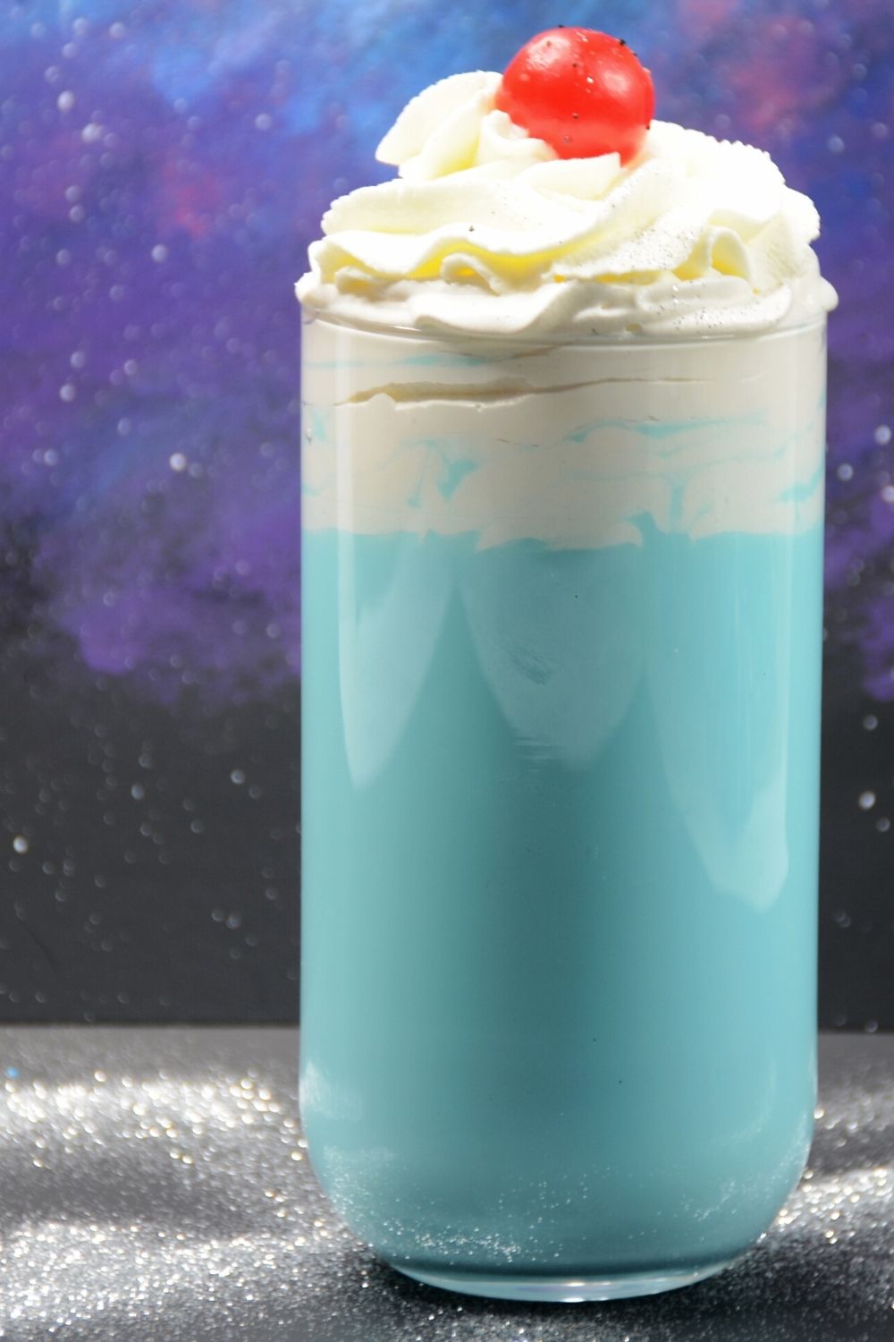 side view of a glass of copycat star wars blue milk garnished with whipped cream and cherry. 