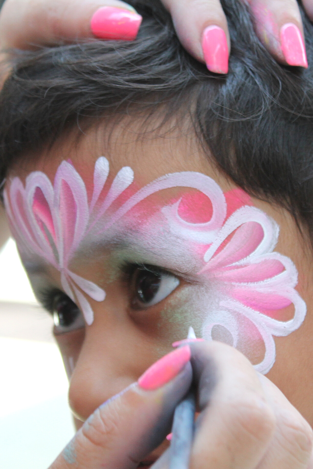 a child gets their face painting with a pink design at disney world