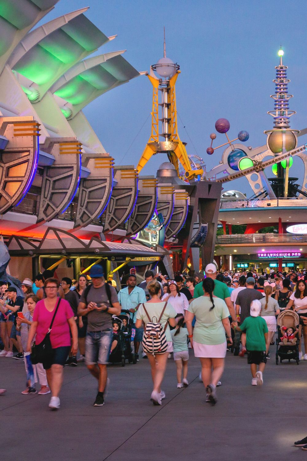 Disney guests walk around Tomorrowland in Magic Kingdom at dusk